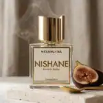 Elegant Nishane Wulong Cha perfume bottle with a gold cap, accompanied by fresh fig halves on a marb.