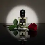 Amouage Rose Agor perfume bottle with a red rose and green leaves, reflected on a glossy surface.