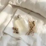 Luxurious perfume bottle with decorative tassel and natural elements on white linen.