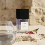 BohoBoco Sea Salt Caramel fragrance bottle with black cap on a rustic surface with pink peppercorns.