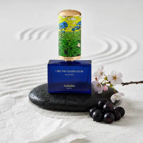 FloraiKu I See the Clouds Go By perfume bottle with artistic design, set on a black stone with cherr.