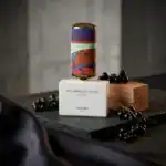 Floraiku fragrance bottle with artistic design, displayed on a wooden block with black berries.