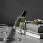 Alwa Aqua perfume bottle with black cap, placed on books with pistachios in a bowl, on a gray backgr.