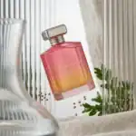 Osmonde Jayne Sakura fragrance bottle with pink and orange gradient, elegant cap, surrounded by gree.