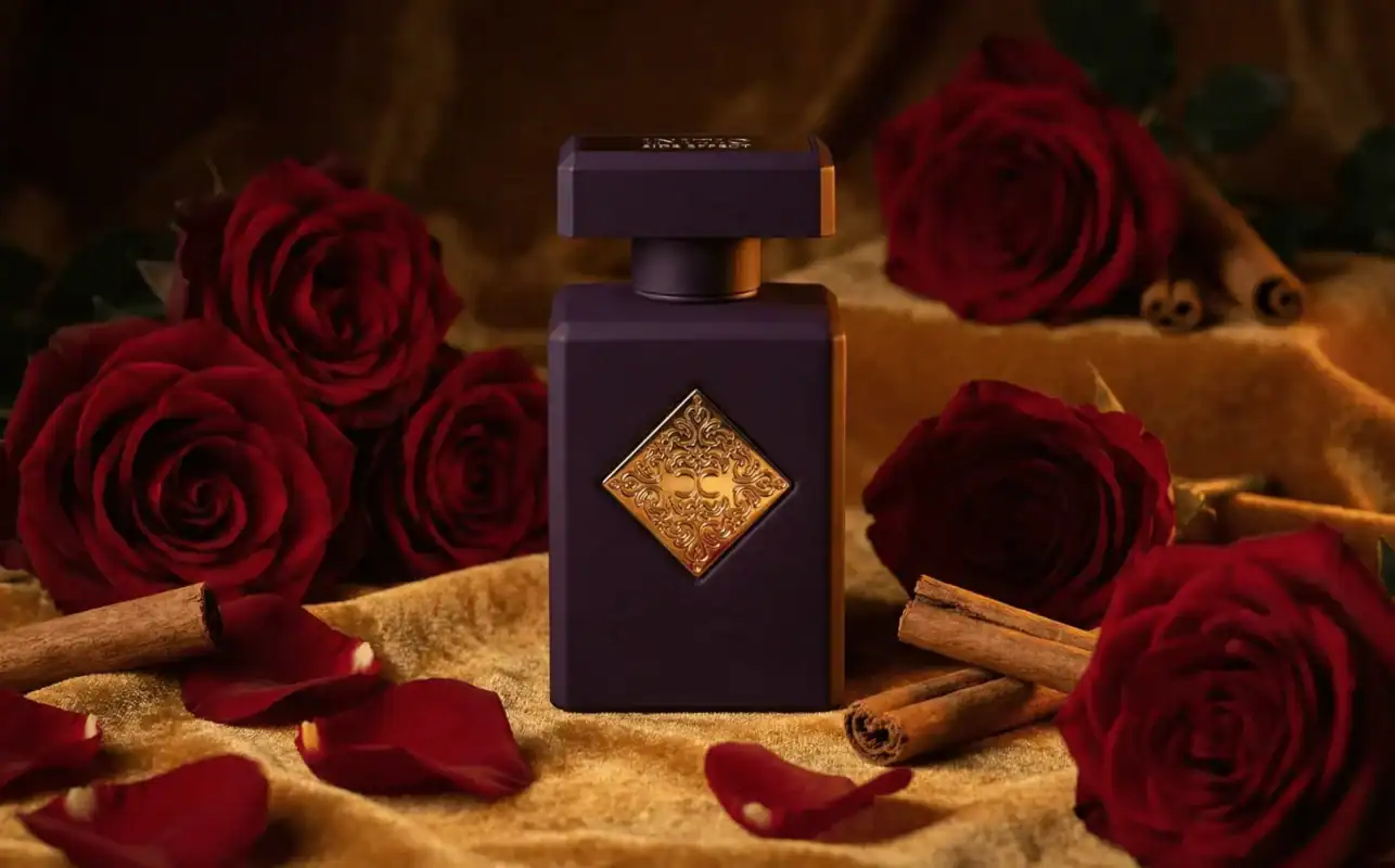 Elegant dark perfume bottle with ornate gold embellishments set against rich red roses and cinnamon, capturing luxury and sophistication.