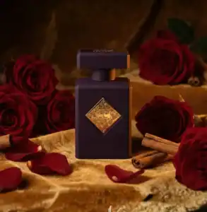 Luxurious dark perfume bottle with gold accents surrounded by red roses and cinnamon sticks.