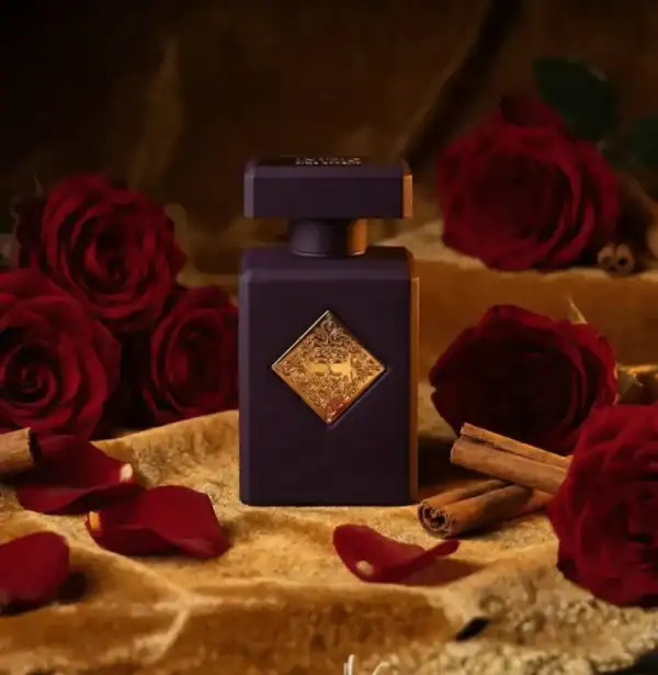 Luxurious dark perfume bottle with gold accents surrounded by red roses and cinnamon sticks.