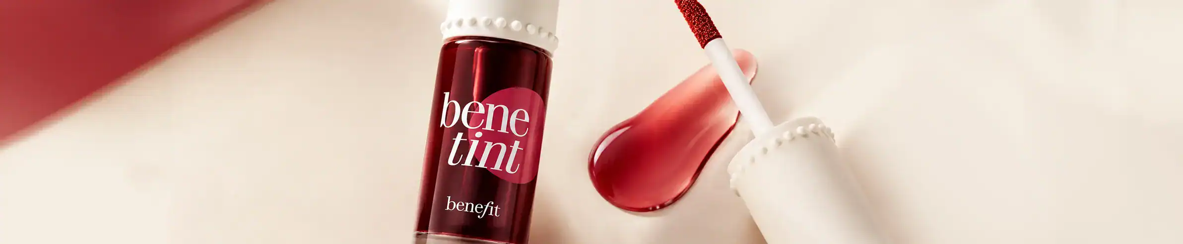 Benefit Tinte lip gloss with applicator wand in a luxurious red hue.