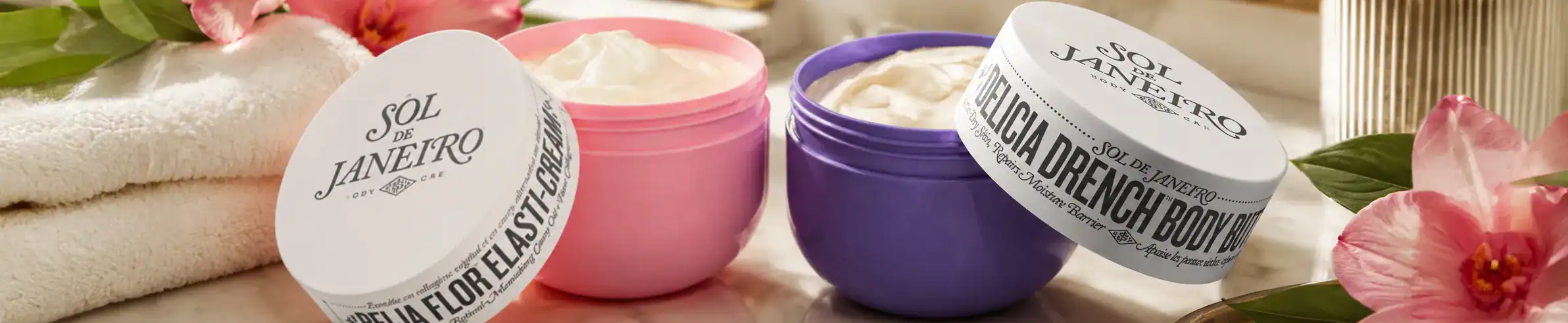 Sol de Janeiro body cream collection with colorful jars and floral accents.
